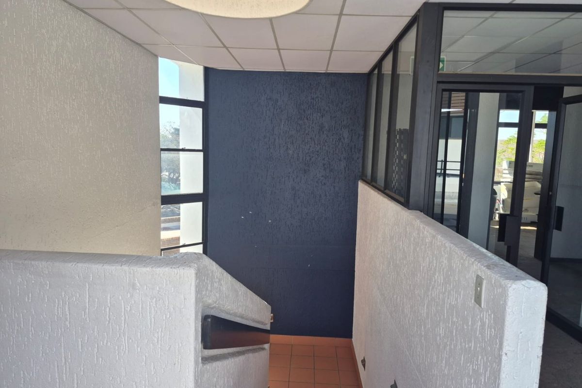 A commercial hallway featuring a staircase with a handrail, textured wall finishes, and a glass partition leading to an adjacent office space.