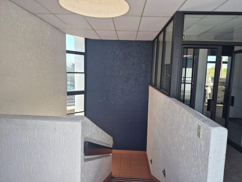 A commercial hallway featuring a staircase with a handrail, textured wall finishes, and a glass partition leading to an adjacent office space.