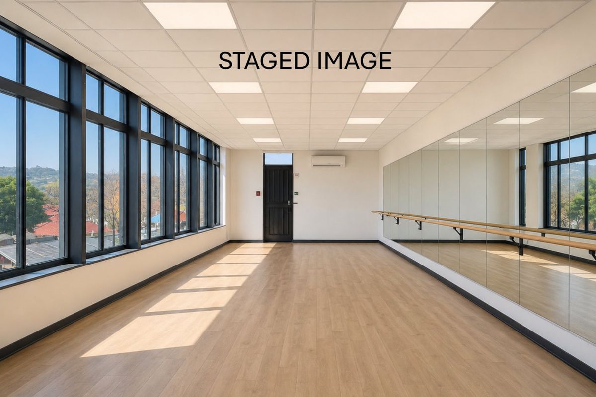 A bright, modern studio space featuring laminate flooring, full-length wall mirrors, a ballet barre, and large windows providing ample natural light.