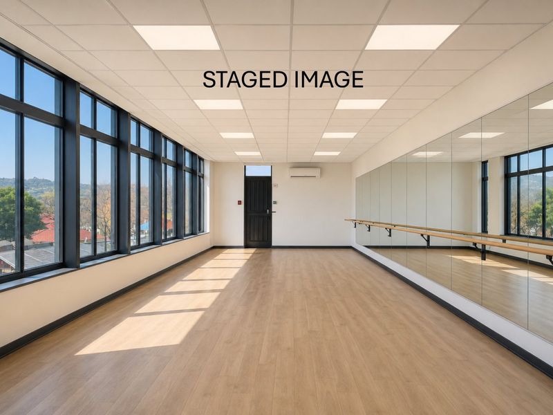 A bright, modern studio space featuring laminate flooring, full-length wall mirrors, a ballet barre, and large windows providing ample natural light.