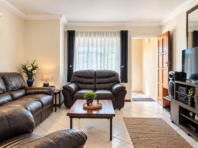 A well-maintained living room featuring tiled flooring, cove cornicing, and direct access to an outdoor area through a timber door.