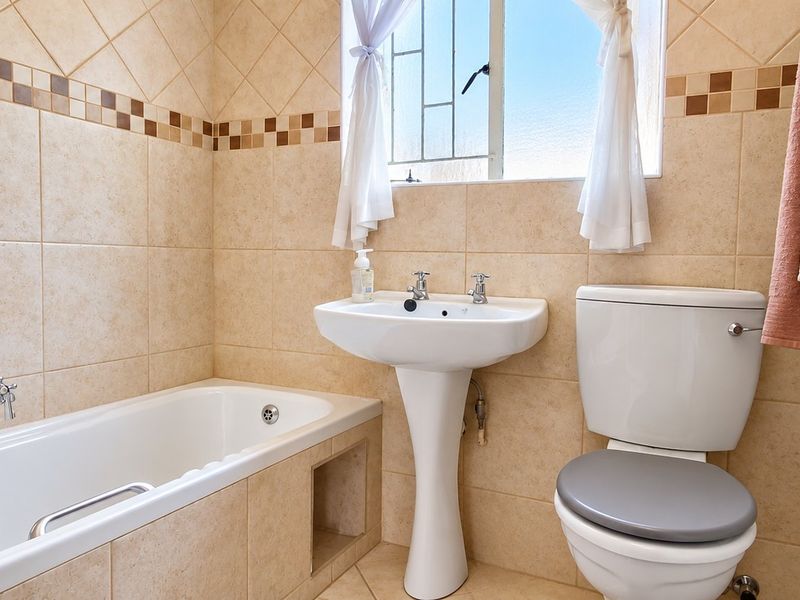 A functional bathroom featuring a pedestal basin, built-in bathtub, and toilet, finished with neutral wall and floor tiling.