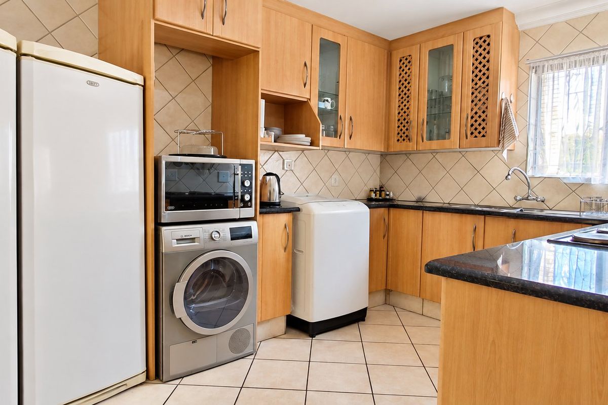 Functional kitchen featuring laminate cabinetry, granite countertops, tiled backsplash, and integrated laundry facilities with a practical layout.