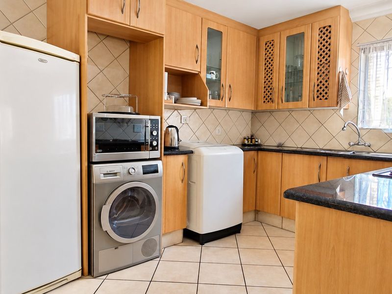 Functional kitchen featuring laminate cabinetry, granite countertops, tiled backsplash, and integrated laundry facilities with a practical layout.