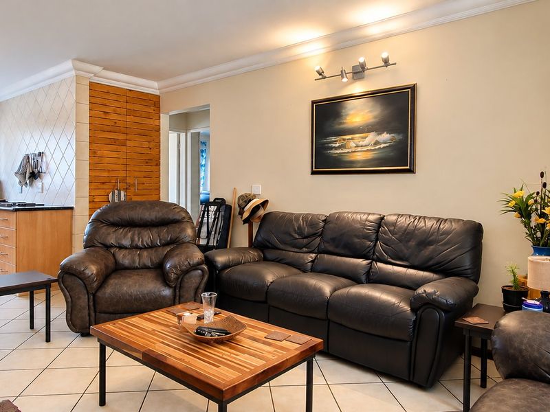 Open-plan living area featuring a functional kitchen with built-in cabinetry, oven, and hob, seamlessly connected to a comfortable lounge space with tiled flooring.