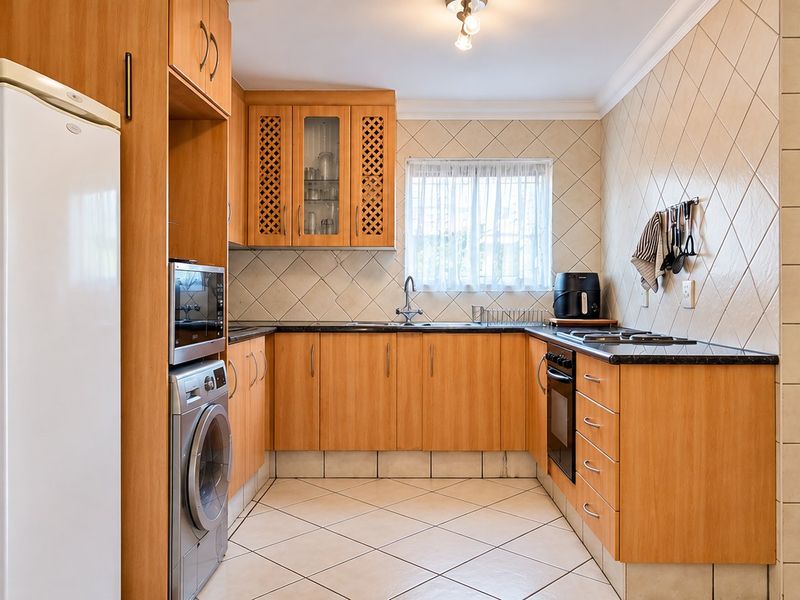A functional kitchen featuring wood-finish cabinetry, laminate countertops, built-in oven and hob, tiled backsplash, and tiled flooring.