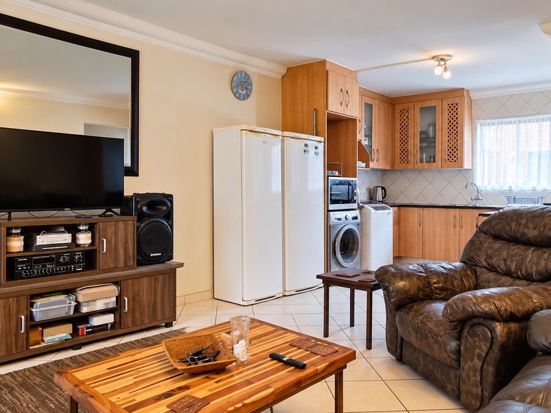 Open-plan living area featuring tiled floors, timber wall accents, and a functional kitchen with built-in cabinetry and integrated appliances.