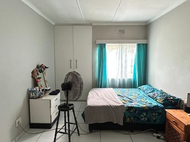 A functional bedroom featuring built-in wardrobes, tiled flooring, and a window allowing natural light.