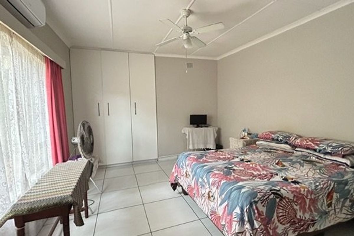 A spacious bedroom featuring tiled flooring, built-in cupboards, a ceiling fan, and an air conditioning unit.