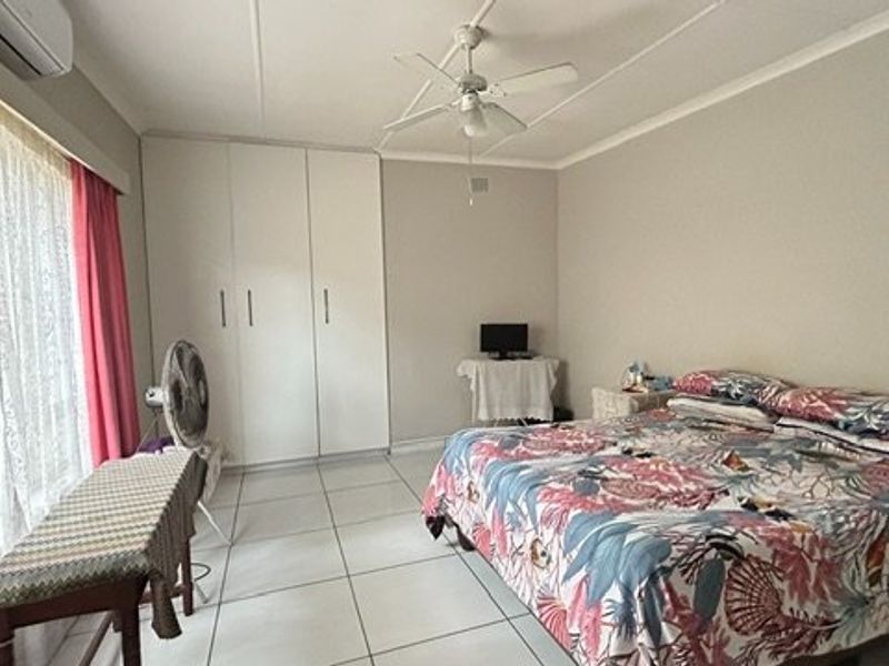 A spacious bedroom featuring tiled flooring, built-in cupboards, a ceiling fan, and an air conditioning unit.