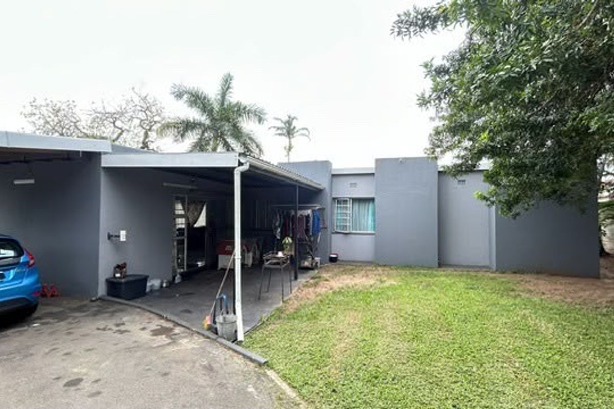 Rear view of the property featuring a covered patio area, paved driveway, and a private garden space.