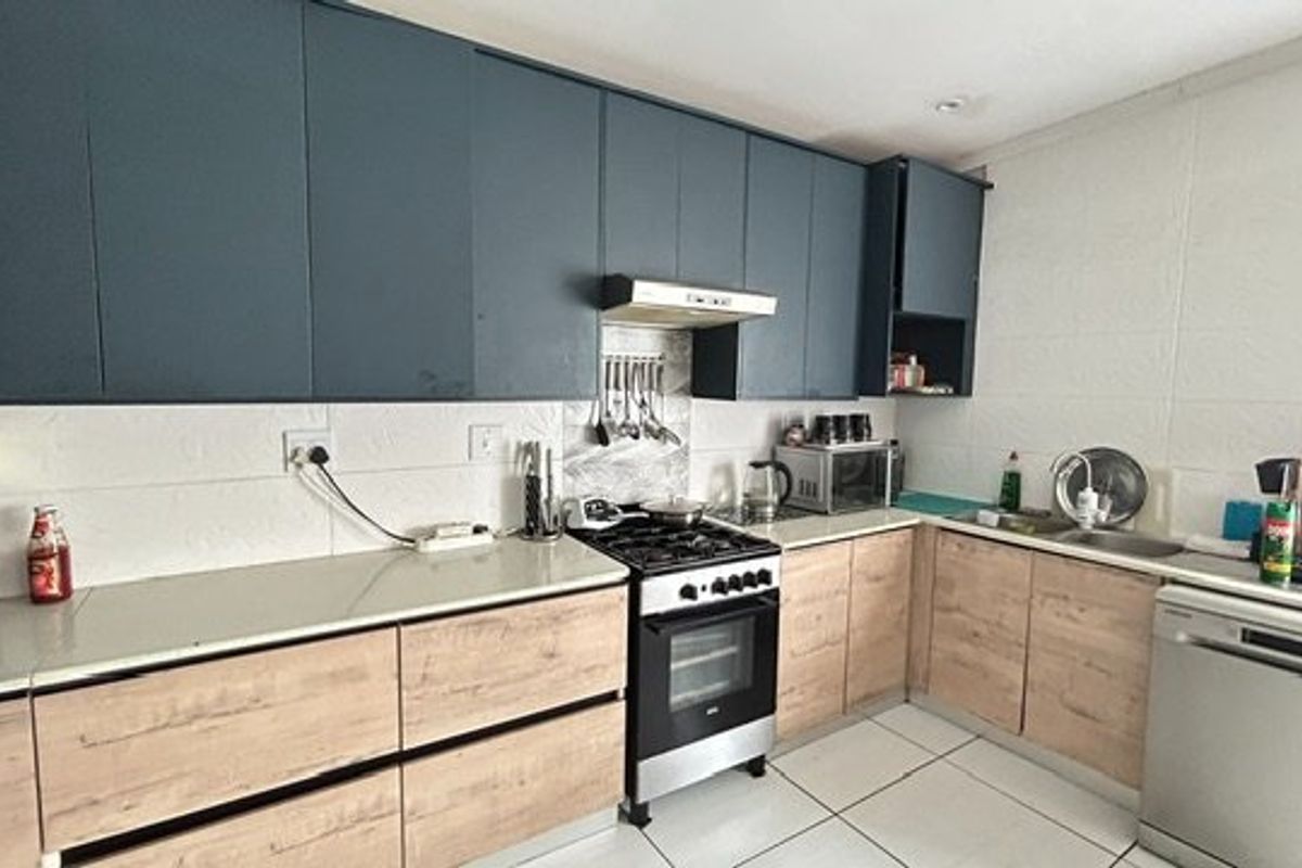 Modern kitchen featuring dark upper cabinetry, light wood-look lower cabinets, stone countertops, gas stove with extractor, and tiled flooring.