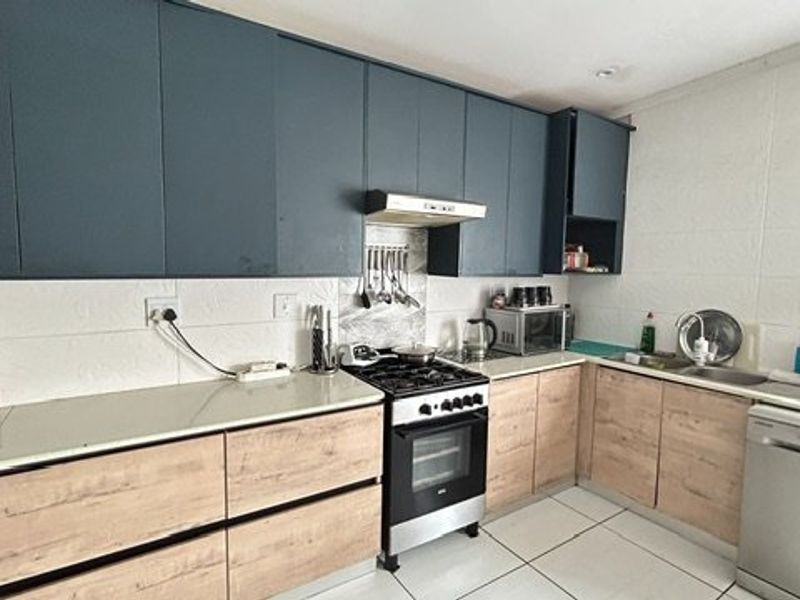 Modern kitchen featuring dark upper cabinetry, light wood-look lower cabinets, stone countertops, gas stove with extractor, and tiled flooring.