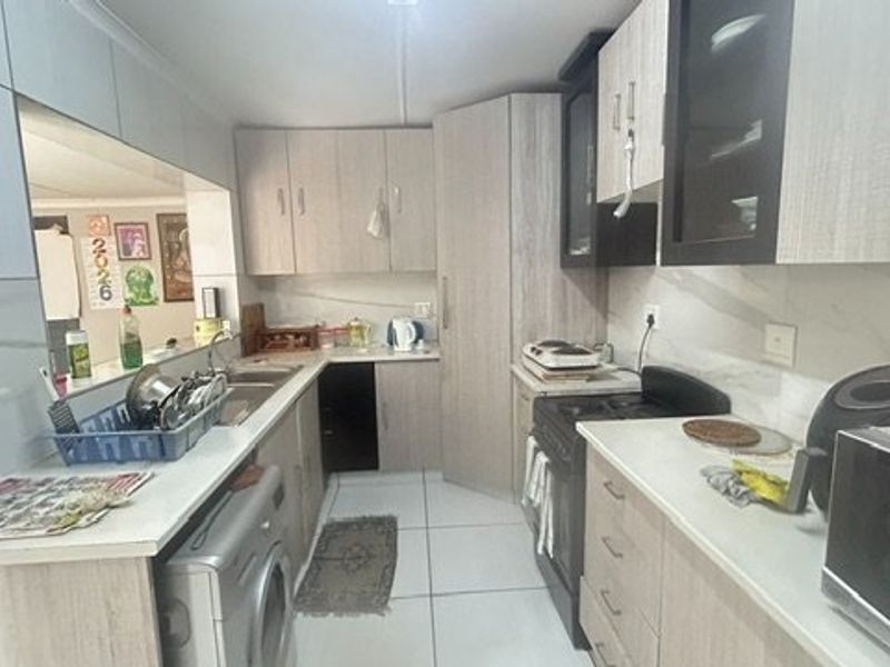 A functional kitchen featuring light wood-finish cabinetry, laminate countertops, a double sink, and a freestanding stove with tiled backsplash and flooring.