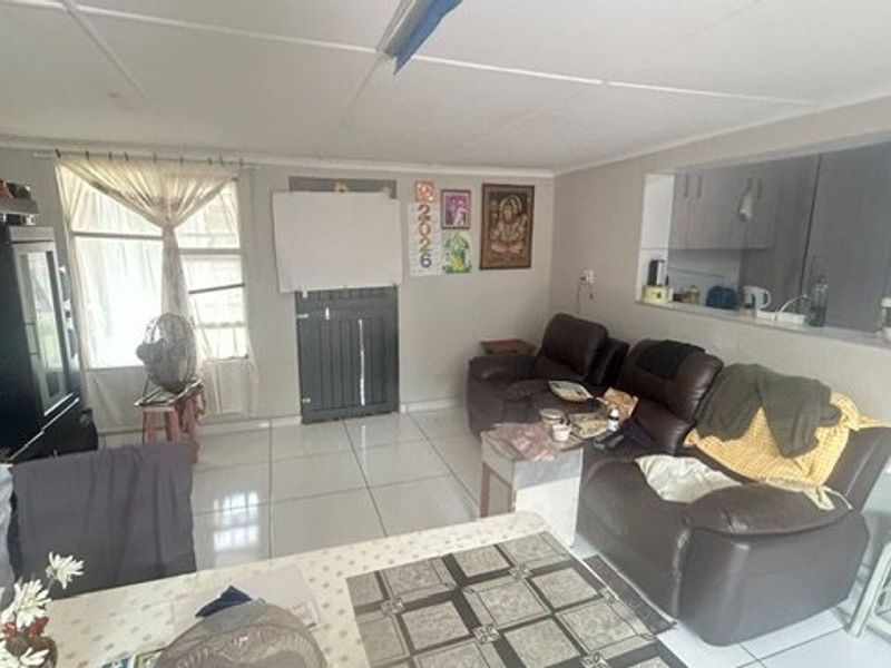 Open plan living area featuring tiled flooring and a kitchen pass-through window, providing a functional layout with potential for cosmetic updates.