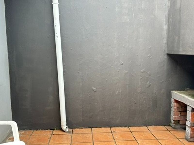 A compact outdoor patio area featuring tiled flooring and a built-in brick braai, requiring some maintenance to the wall finish.