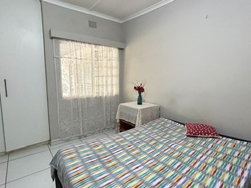 A functional bedroom featuring built-in cupboards, tiled flooring, and a window fitted with security bars.