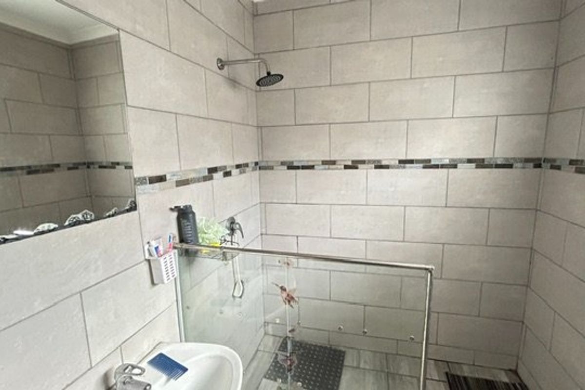 A modern bathroom featuring a walk-in shower with a glass screen, tiled walls with a decorative mosaic border, and a wall-mounted mirror.