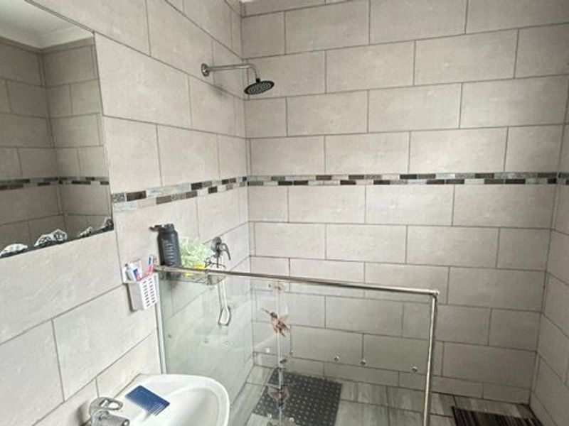 A modern bathroom featuring a walk-in shower with a glass screen, tiled walls with a decorative mosaic border, and a wall-mounted mirror.