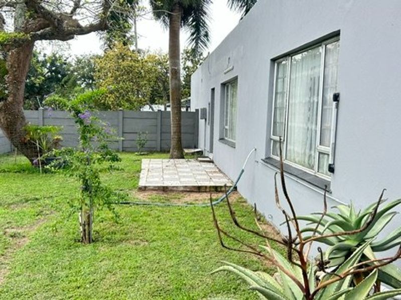 Rear exterior view of the property featuring a lawn, a small tiled patio area, and a precast concrete boundary wall.