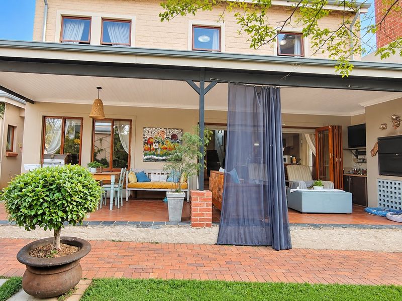 A spacious covered patio featuring tiled flooring, a built-in braai, and bi-fold doors leading into the home, overlooking a brick-paved garden area.