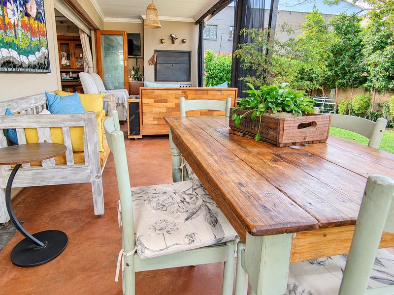 A covered outdoor patio featuring a built-in braai, concrete flooring, and seamless access to the garden through large sliding doors.