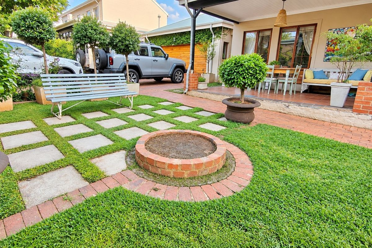 A well-maintained rear garden featuring a brick fire pit, stone paver pathway, and a covered patio area.