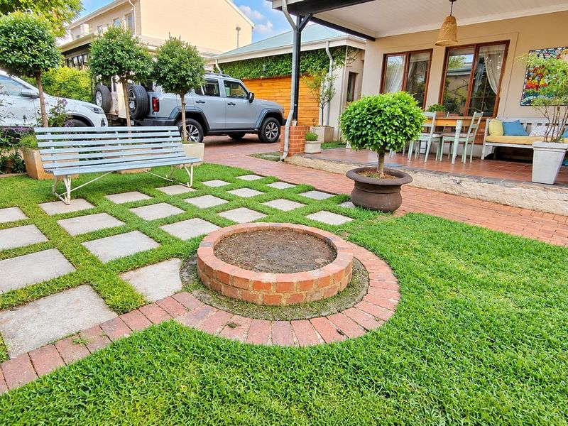 A well-maintained rear garden featuring a brick fire pit, stone paver pathway, and a covered patio area.