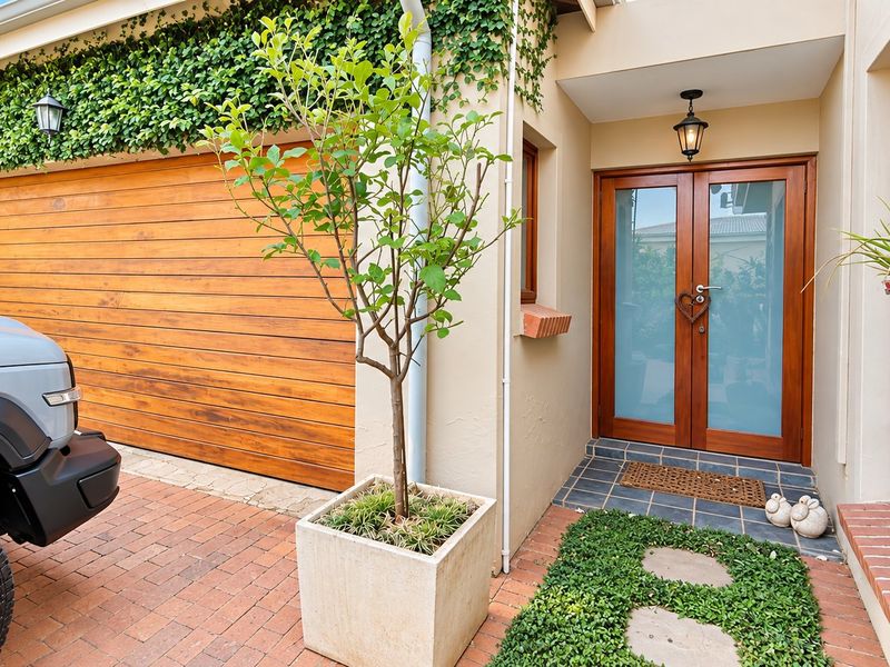 A well-maintained front entrance featuring a timber garage door, double glass entry doors, and brick paving.