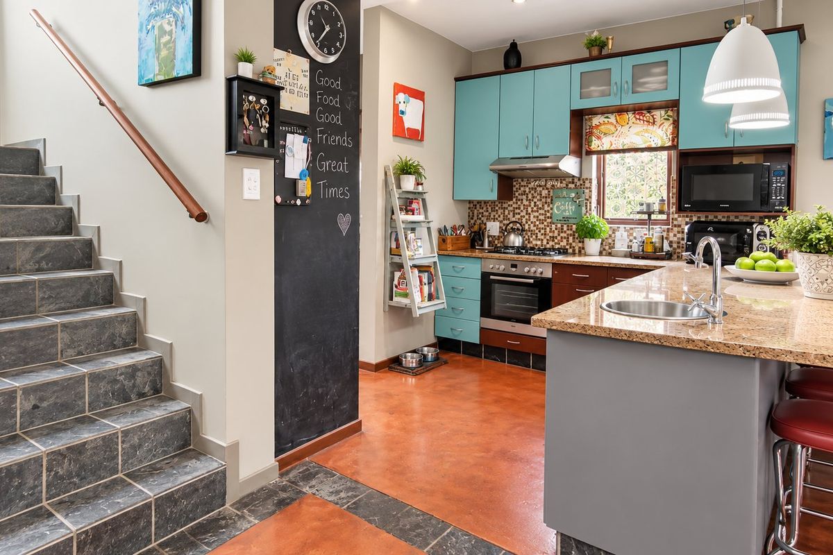 Modern kitchen featuring a granite island, built-in appliances, and a unique chalkboard wall, adjacent to a tiled staircase with a wooden handrail.