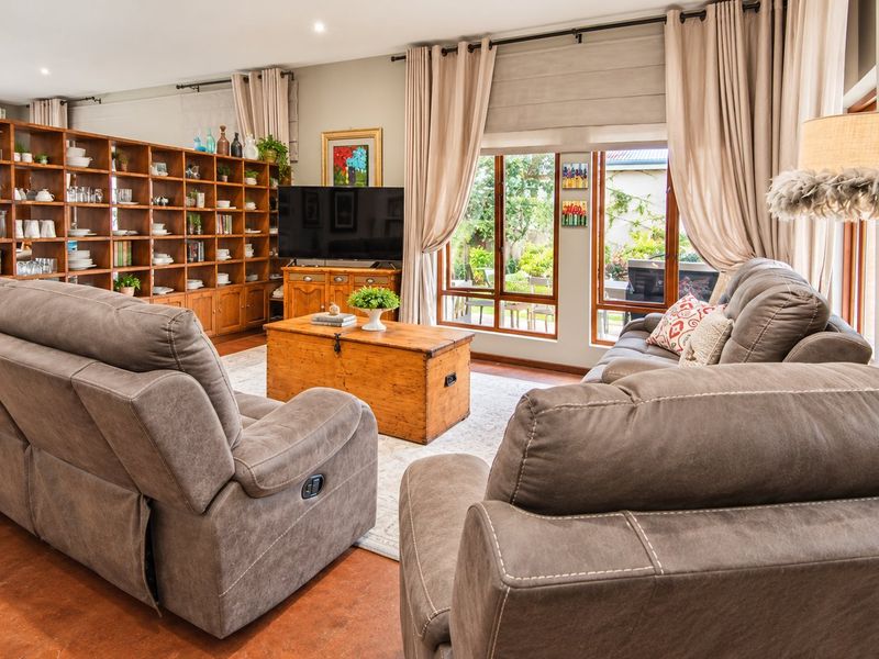 A spacious living room featuring polished concrete floors, recessed lighting, and a large built-in wooden shelving unit with direct access to the garden.