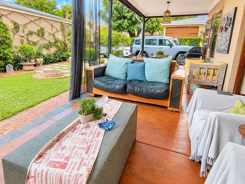 A covered outdoor patio area featuring concrete flooring, overlooking a landscaped garden with brick paving and a retaining wall.
