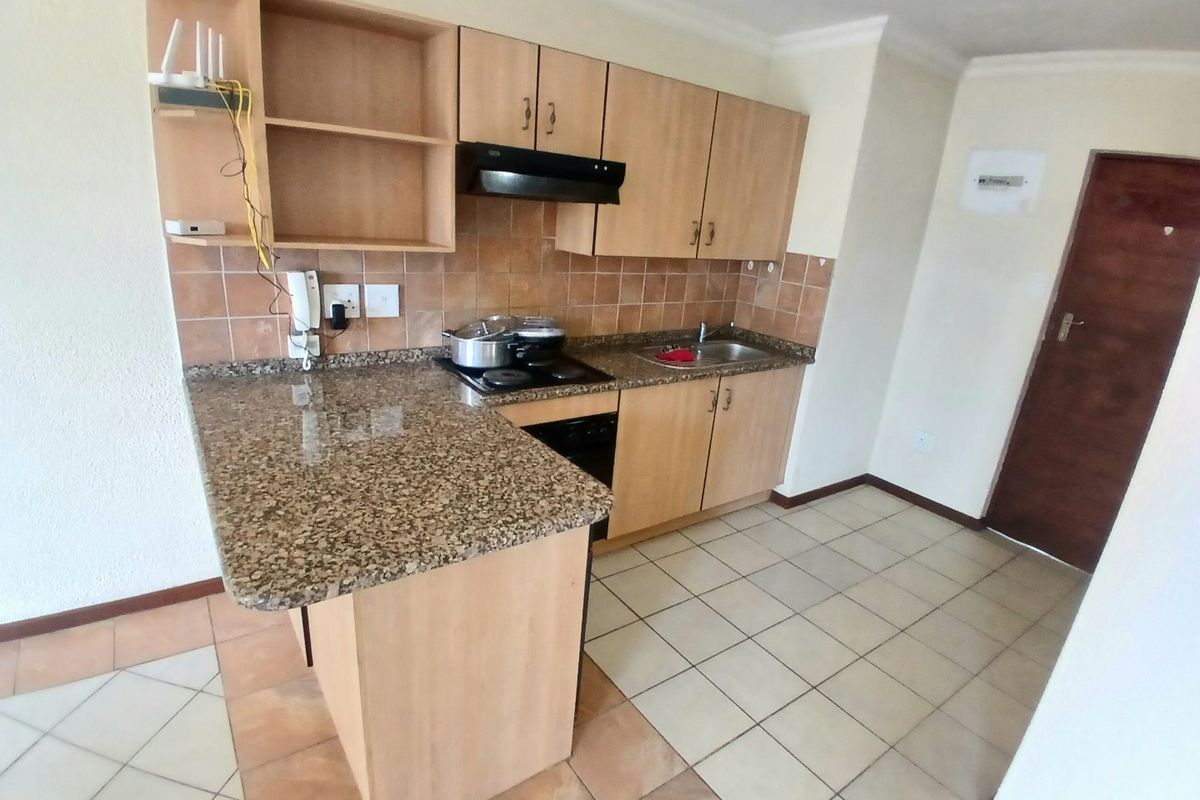 A functional kitchen featuring granite countertops, built-in wooden cabinetry, an electric hob with extractor fan, and tiled flooring.