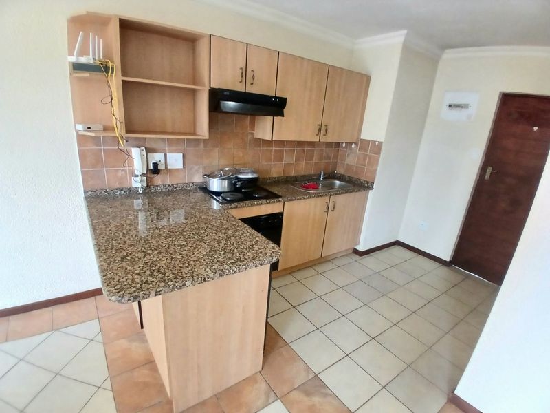 A functional kitchen featuring granite countertops, built-in wooden cabinetry, an electric hob with extractor fan, and tiled flooring.