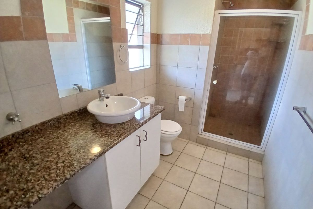 A functional bathroom featuring a granite vanity countertop, vessel sink, shower enclosure, and neutral ceramic tiling throughout.