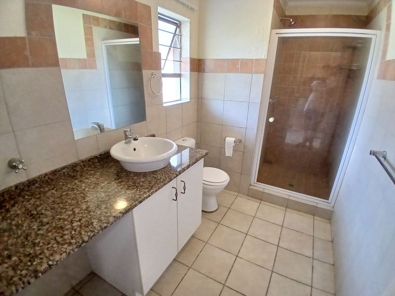 A functional bathroom featuring a granite vanity countertop, vessel sink, shower enclosure, and neutral ceramic tiling throughout.
