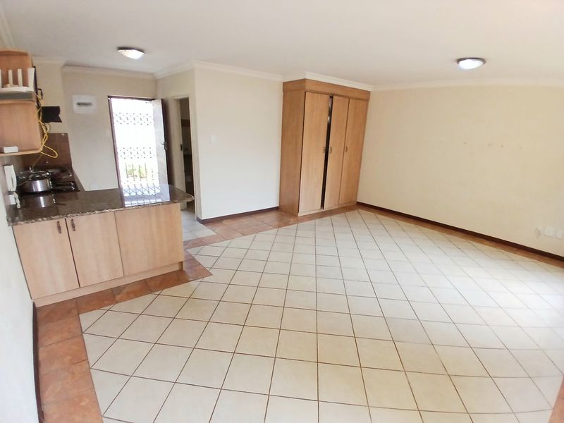 Open-plan living area featuring tiled flooring, built-in kitchen cabinetry with granite countertops, and a built-in wardrobe for storage.