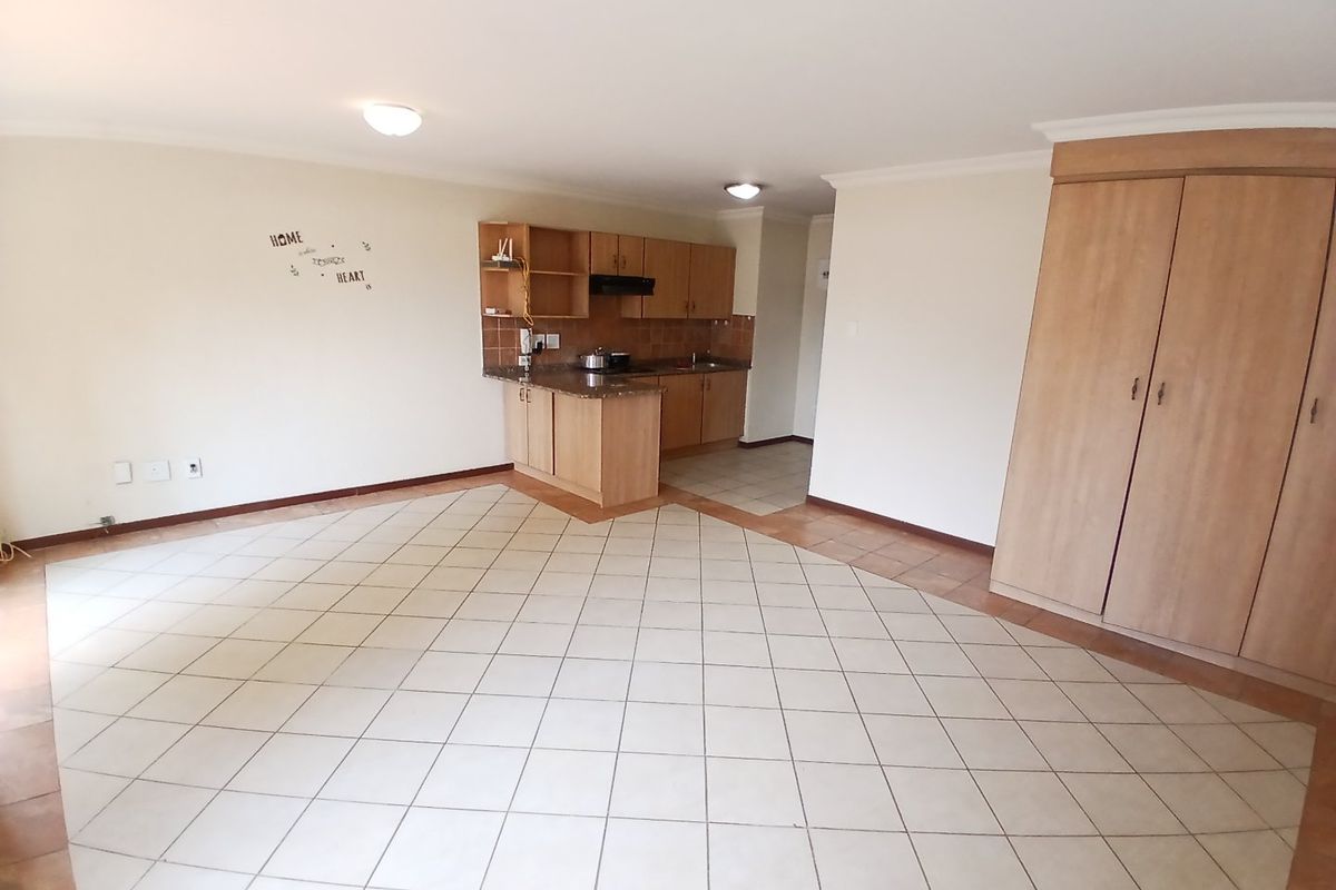 Open-plan living area featuring tiled flooring, built-in kitchen cabinetry with laminate countertops, and a large built-in storage cupboard.