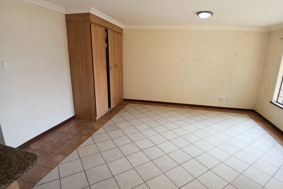An empty bedroom featuring tiled flooring, a built-in wooden wardrobe, and neutral wall finishes.
