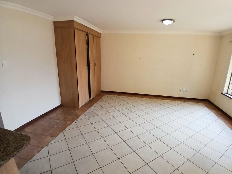 An empty bedroom featuring tiled flooring, a built-in wooden wardrobe, and neutral wall finishes.
