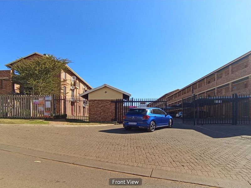 Exterior view of the apartment complex entrance featuring brick facade buildings, paved driveway, and secure gated access.
