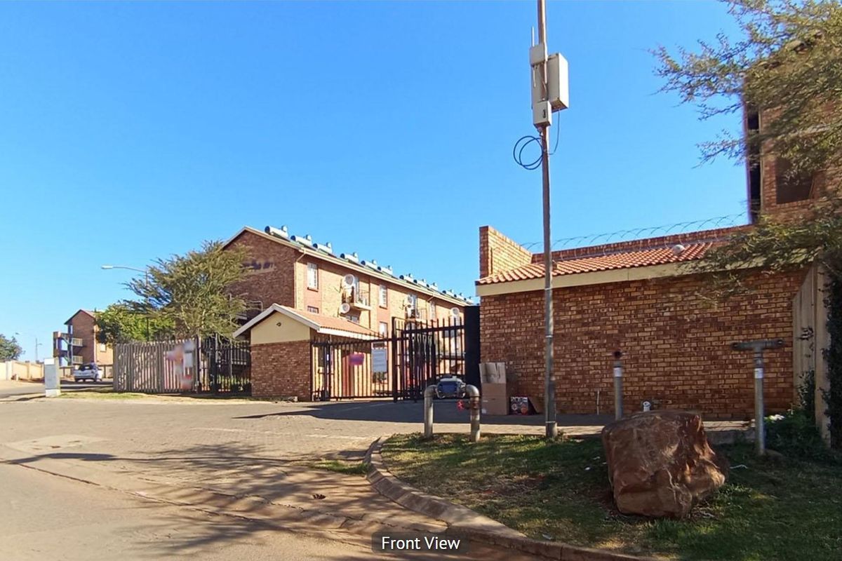 Street-level view of the apartment complex entrance, featuring face brick construction, secure gated access, and perimeter fencing with razor wire.