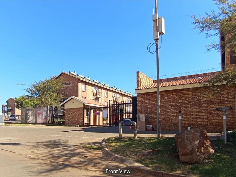 Street-level view of the apartment complex entrance, featuring face brick construction, secure gated access, and perimeter fencing with razor wire.