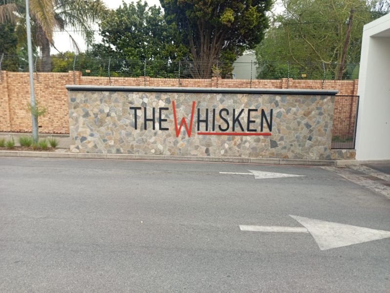 The entrance to The Whisken apartment complex, featuring a stone-clad signage wall, electric fencing, and a paved driveway.