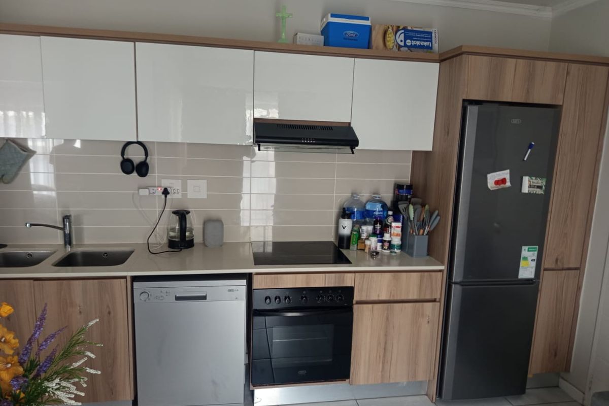 Modern kitchen featuring wood-grain and white cabinetry, integrated appliances including a hob, oven, and extractor fan, complemented by a tiled backsplash.