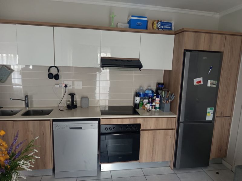 Modern kitchen featuring wood-grain and white cabinetry, integrated appliances including a hob, oven, and extractor fan, complemented by a tiled backsplash.