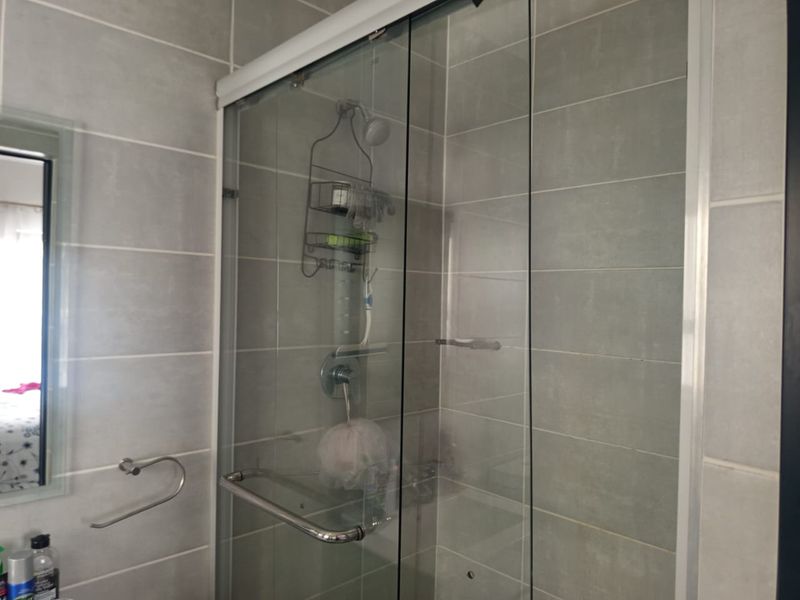 A modern bathroom featuring a glass-enclosed shower with grey wall tiling and chrome fixtures.