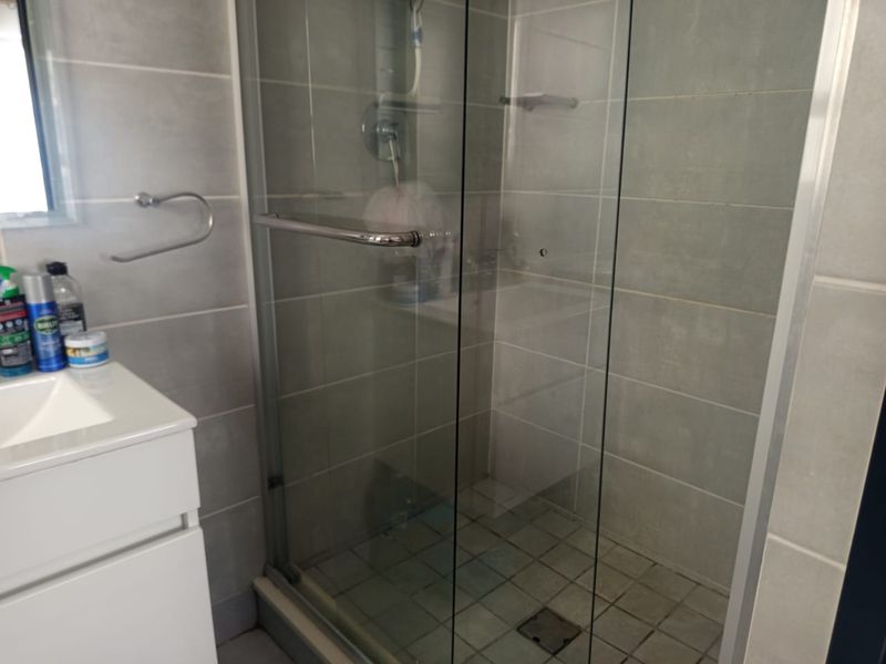 A functional bathroom featuring a glass-enclosed shower, tiled walls and flooring, and a modern vanity cabinet.