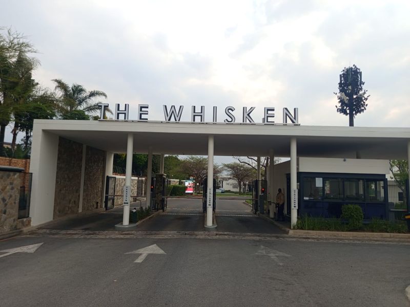 The main entrance and security gatehouse of The Whisken apartment complex, featuring a modern structure with boom gates and clear signage.