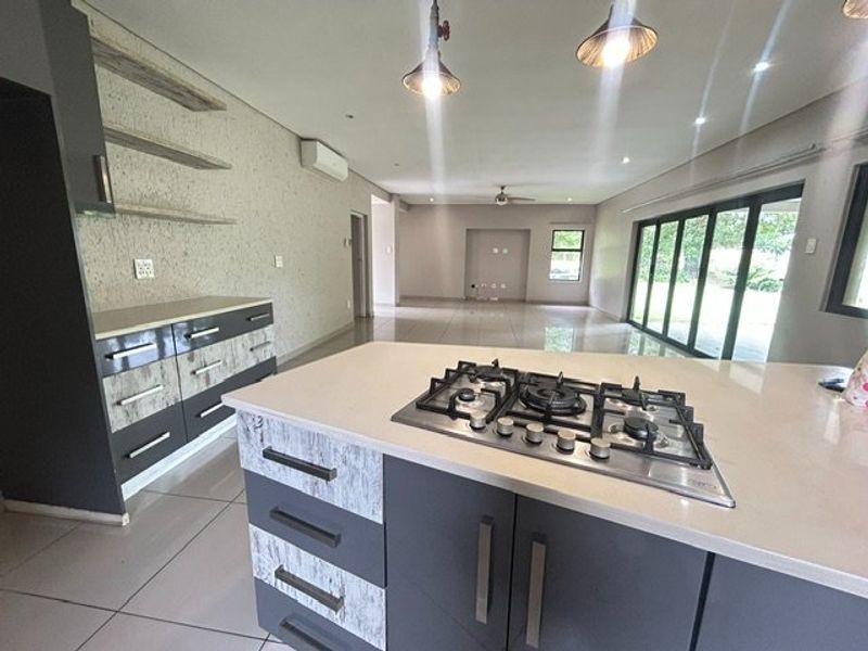 Spacious open-plan living area featuring a modern kitchen with a central island, gas cooktop, stone countertops, and seamless flow to the outdoor patio.